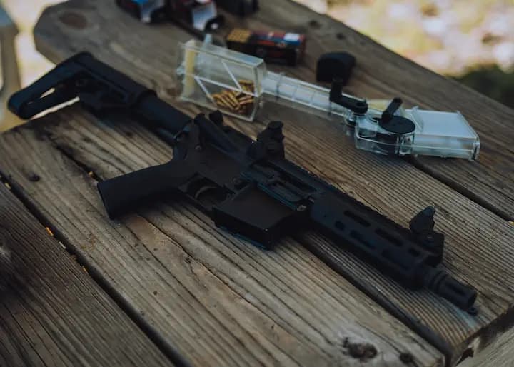 Close-up of a Tippmann Arms rifle with a sleek black finish, resting on a rustic wooden surface, accompanied by reloading tools and ammunition, perfect for showcasing quality and craftsmanship.